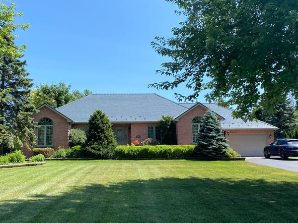 Single-storey brick ranch home in Cornwall, ON with a deep charcoal Interlock aluminum slate hip roof, two-car garage, and manicured lawn.