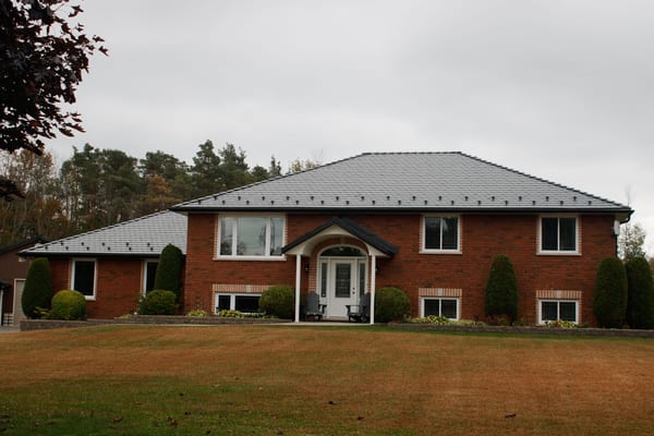 Two-storey red brick Colonial home in Carrying Place, ON with a medium-pitch hip roof clad in black Interlock aluminum slate tiles.