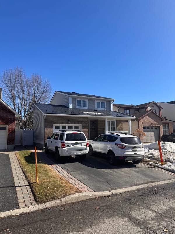 Two-storey brick Colonial home in Orleans ON fitted with black Interlock aluminum slate metal roofing, featuring a front dormer and attached garage.
