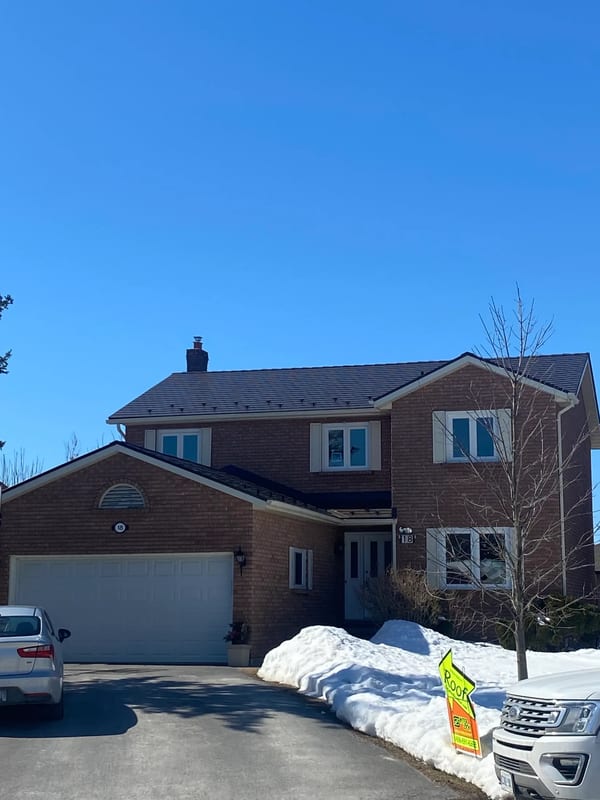 Two-storey brick Colonial home in Belleville ON with Interlock Tudor Brown aluminum slate metal roof, chimney, and snow guards on a clear winter day.