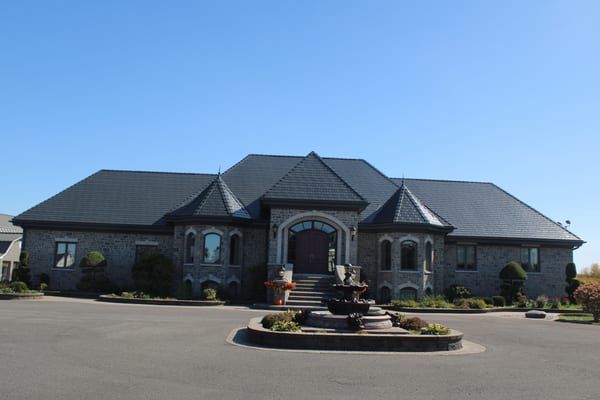 Grand single-storey stone estate in Alexandria ON featuring Interlock deep charcoal aluminum slate roofing with turreted hip roof and circular fountain driveway.