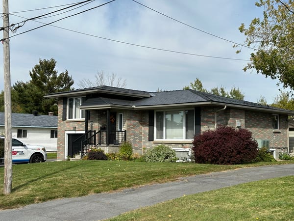 Raised ranch brick home in Cornwall ON with a black Interlock aluminum slate hip roof, low pitch, black gutters, and mature fall trees.