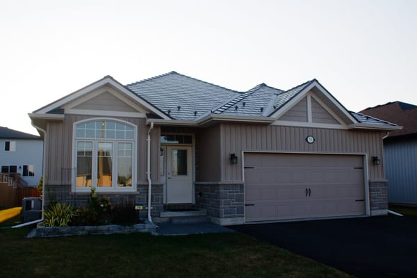 Single-family ranch-style home in Belleville ON with Interlock Tudor Brown aluminum slate metal roofing featuring multi-hip complex roof profile and stone accent base.