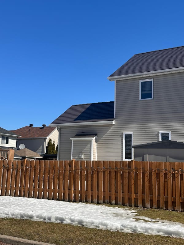 Tudor Brown Interlock aluminum slate metal roof on a two-storey suburban home in Ottawa, viewed from rear-left with a wooden fence in the foreground.