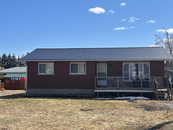 Front elevation of a brick ranch home in Chesterville, ON featuring a black Interlock aluminum slate metal roof with a low-pitch simple gable and front deck.