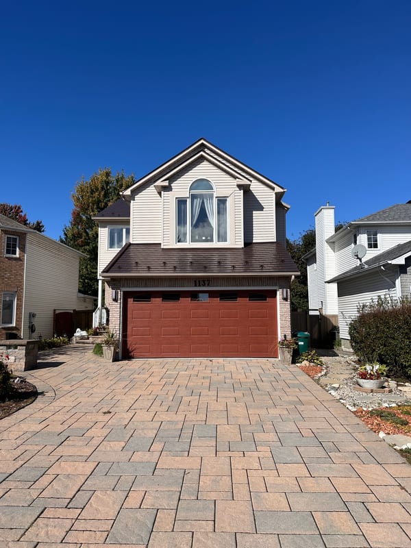 Two-storey suburban home with Interlock Colonial Brown aluminum slate roof, brown gable profile, arched dormer window, and interlocking paver driveway.