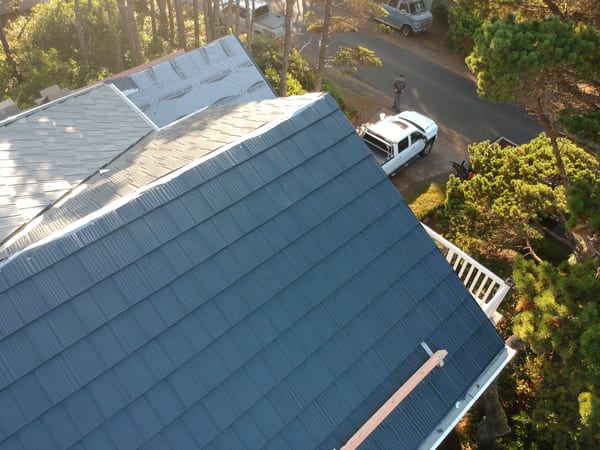 Aerial view of a multi-plane Deep Charcoal Interlock aluminum shake metal roof on a forested single-family home in Lincoln City, OR.