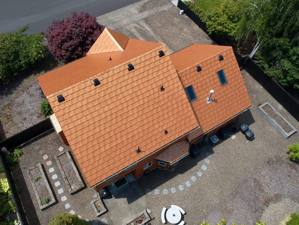 Aerial view of a two-story home in Albany, OR featuring Interlock aluminum shake roofing in Copper Penny with multiple hips, skylights, and roof vents.