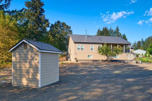 Rear elevation of a ranch-style home in Lebanon, OR featuring Interlock black aluminum slate metal roofing with a medium-pitch gable profile and detached storage shed.