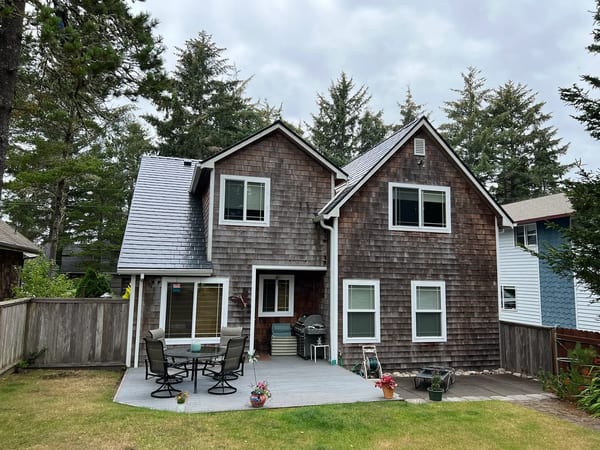 Rear elevation of a two-story cedar-shingle cottage in Manzanita, OR featuring Interlock aluminum slate roofing in Deep Charcoal with complex multi-gable rooflines.