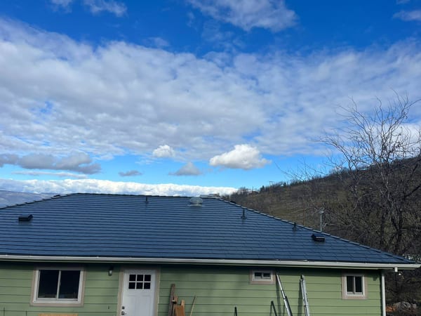 Deep charcoal Interlock aluminum slate metal roof on a single-story ranch-style home with green siding, set against a hillside in The Dalles, OR.
