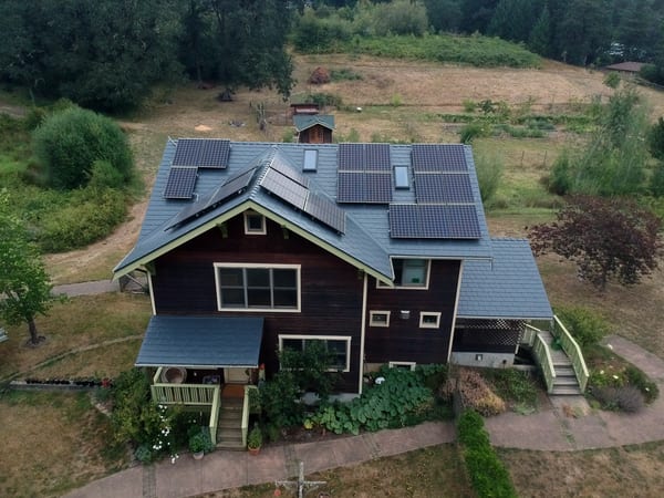 Aerial view of a 2-story Craftsman home in Corvallis, OR with a complex deep charcoal Interlock aluminum slate roof featuring multiple solar panels and skylights.