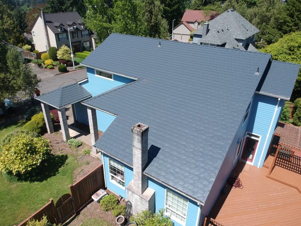 Aerial view of a two-story blue home in Gresham, OR with a complex multi-hip Interlock aluminum slate roof in Deep Charcoal.