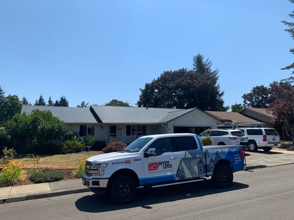 Street view of a single-story Ranch home in Salem, OR with an Interlock Deep Charcoal aluminum cedar shingle metal roof, with an Interlock-branded truck parked in front.