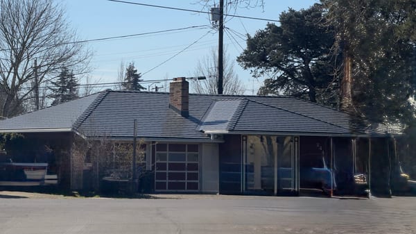 Single-story ranch home in Salem, OR with a complex hip roof in Interlock deep charcoal aluminum slate, featuring a brick chimney and valley intersections.
