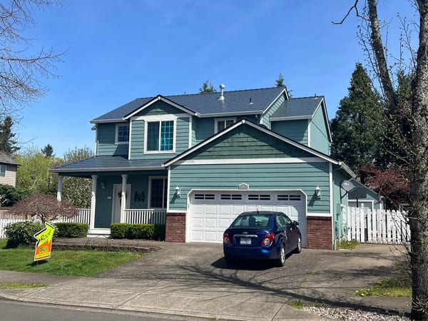 Two-story Craftsman home in Oregon City with deep charcoal Interlock aluminum slate metal roofing, white trim, teal siding, and brick accent base.