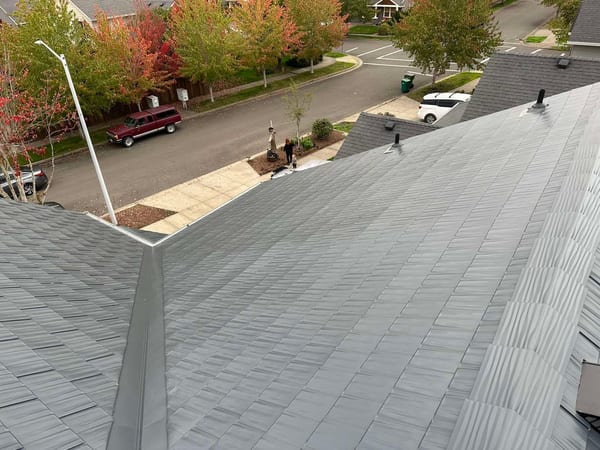 Aerial view of Interlock deep charcoal aluminum cedar shingle metal roof with valley flashing and vent pipes on a two-story suburban home in Newberg, OR.