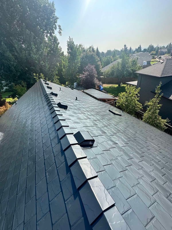 Aerial view of a steep black Interlock aluminum slate metal roof with ridge caps and roof louvers on a Craftsman-style home in Oregon City, OR.