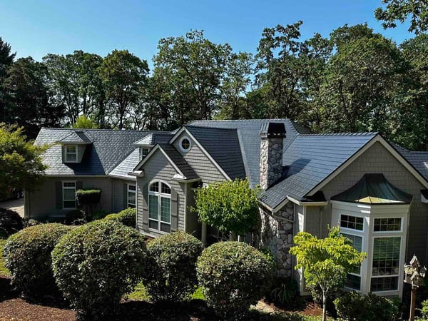 Aerial front view of a Craftsman home in Corvallis, OR with a complex black Interlock aluminum slate metal roof, stone chimney, and dormers.