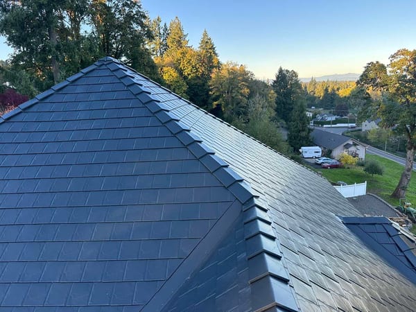 Aerial view of a complex multi-hip black Interlock aluminum slate metal roof with crisp valleys and ridges on a two-story home in Scappoose, OR.