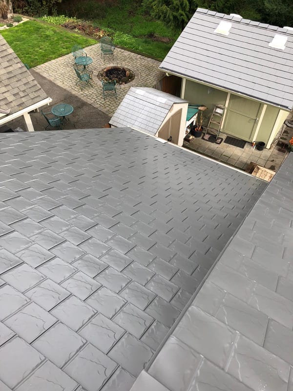 Aerial view of Interlock aluminum slate roof in Musket Grey on a ranch-style home with multiple intersecting planes, skylights, and lush green surroundings.
