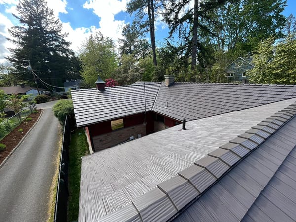 Aerial view of a complex multi-hip Interlock aluminum shake roof in Tudor Brown on a Craftsman-style home surrounded by mature trees in Portland, OR.