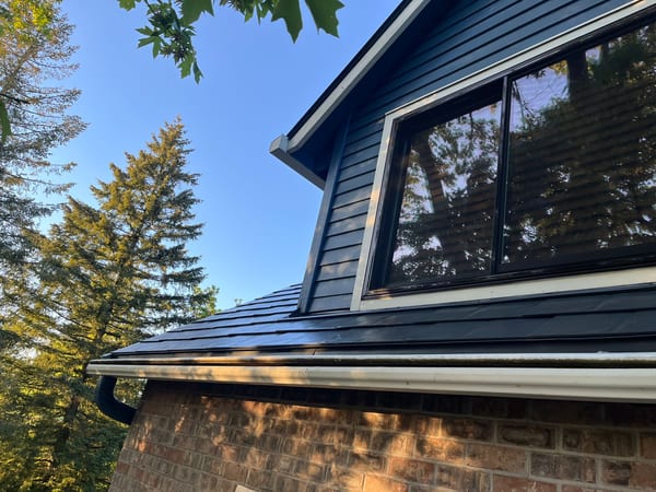 Close-up of a deep charcoal Interlock aluminum slate metal roof on a craftsman home with blue siding, dormer window, and white gutters.