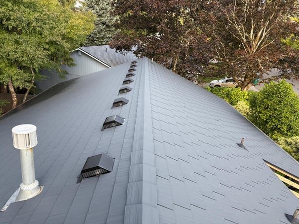 Aerial view of a charcoal Interlock aluminum cedar-shingle metal roof with ridge vents, roof louvers, and vent pipes on a suburban home in Tigard, OR.