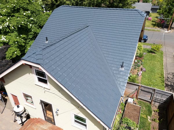 Aerial view of a Craftsman home with Interlock deep charcoal aluminum slate metal roofing, featuring complex multi-plane gable roof and two vent pipes.