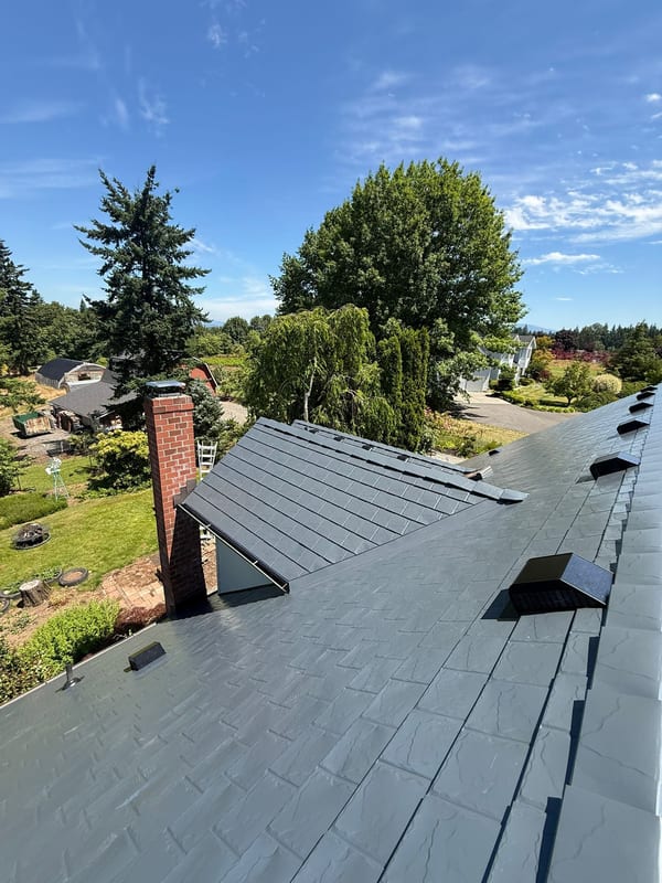 Aerial view of a complex Craftsman home roof clad in Interlock deep charcoal aluminum slate tiles with a red brick chimney and multiple skylights in Gresham, OR.