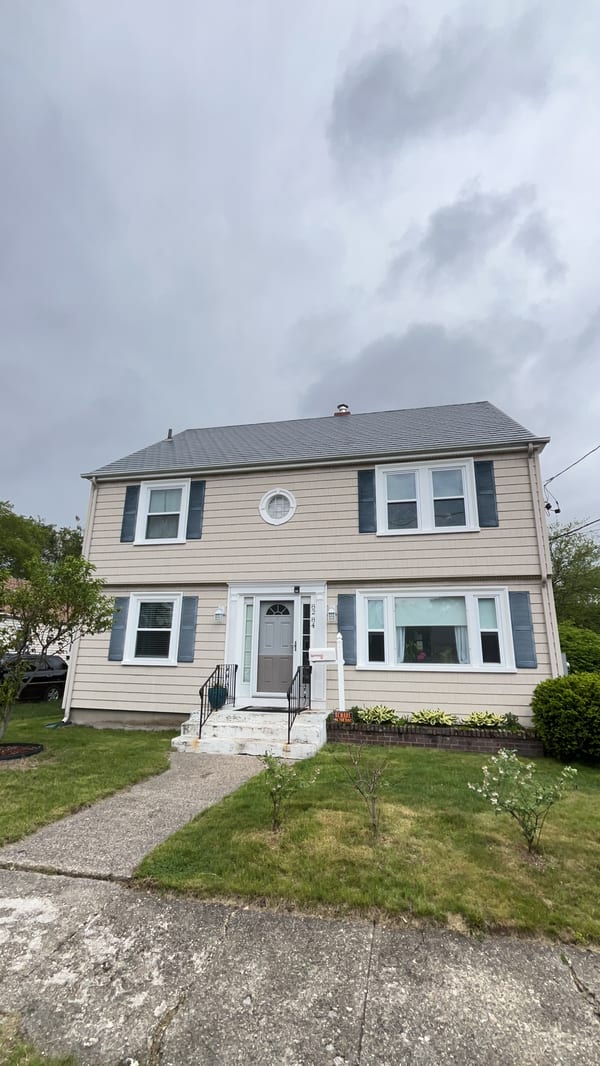 Two-story Colonial home in Pawtucket, RI with Interlock deep charcoal aluminum slate metal roof, dark shutters, and center entry door.
