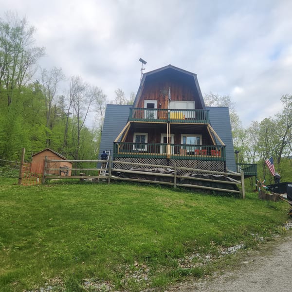 Three-story A-frame cabin in Vermont with hunter green Interlock aluminum shingle roof, multi-tiered decks, and wood siding set against a forested hillside.