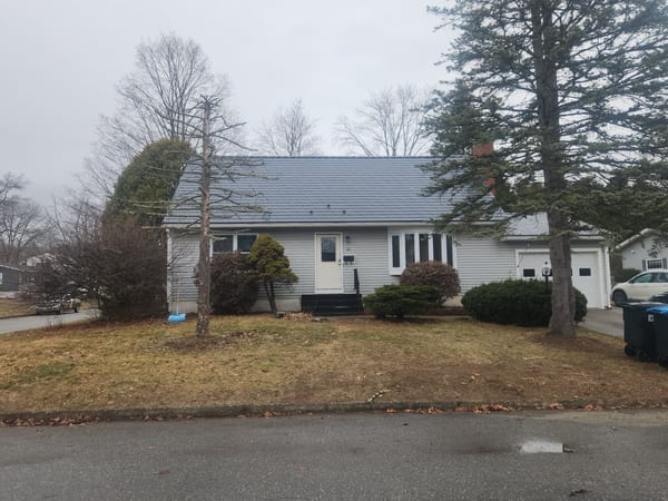 Front elevation of a single-family Ranch home with an Interlock deep charcoal aluminum slate metal roof, attached garage, and brick chimney, South Burlington, VT.