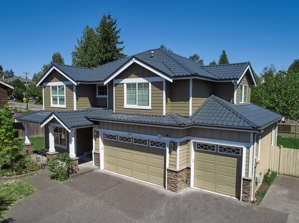 Aerial view of a two-story Craftsman home in Lynnwood, WA with a complex multi-hip Deep Charcoal Interlock Mediterranean tile metal roof and three-car garage.