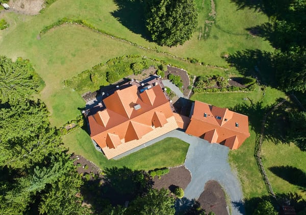 Aerial view of a large single-family home with complex multi-hip Interlock aluminum shake roofing in Copper Penny, surrounded by lush green acreage in Bellingham, WA.