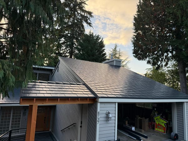 Deep charcoal Interlock aluminum slate metal roof on a 1.5-story Craftsman home in Bellevue WA, showing complex hip lines, chimney, and cedar soffit details.