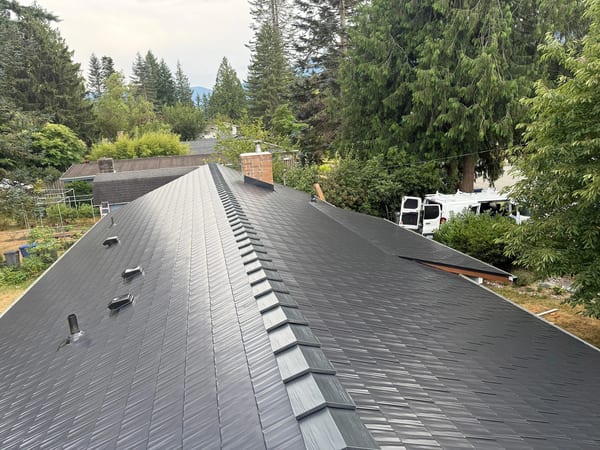 Black Interlock Cedar Shingle aluminum roof on a black two-storey home with a metal roof among tall pines, North Bend, Washington