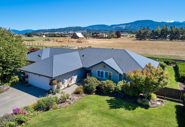 Aerial front view of a ranch-style home in Sequim, WA featuring a complex multi-hip Interlock aluminum slate roof in deep charcoal, with mountain backdrop.