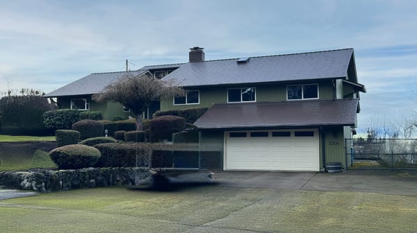 Two-story green ranch-style home in Vancouver WA with Interlock Colonial Brown cedar shingle metal roofing, chimney, and manicured topiary shrubs.
