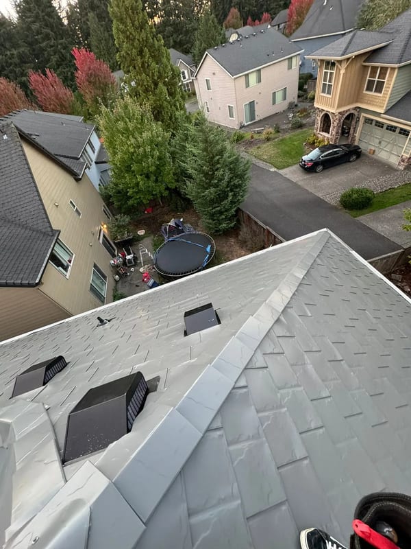 Aerial view of a Craftsman home with Interlock Musket Grey aluminum slate roofing, showing complex hip geometry, ridge caps, and roof vents in a suburban Vancouver, WA neighborhood.
