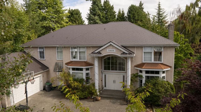 Tudor Brown Interlock Slate aluminum roof on a two-storey Tudor home with dormers among tall trees, Surrey, British Columbia