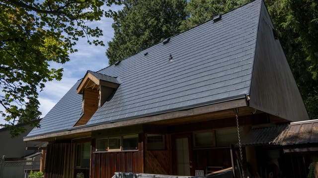Deep Charcoal Interlock Slate aluminum roof on a brown A-frame home with a metal roof among tall trees, Burnaby, British Columbia