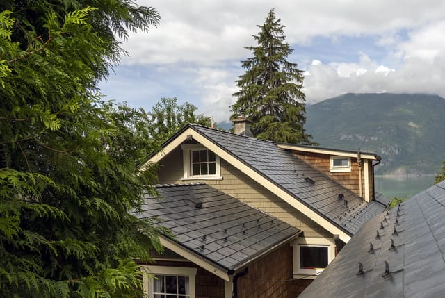 Black Interlock aluminum slate metal roof with multiple dormers and snow guards on a Craftsman home with mountain and water backdrop in Britannia Beach, BC.
