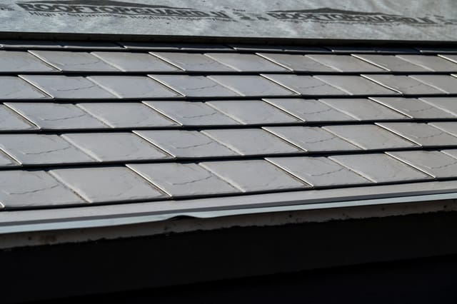 Taupe Interlock Slate aluminum roof on a taupe metal roof on a two-storey home among tall pines, Surrey, British Columbia