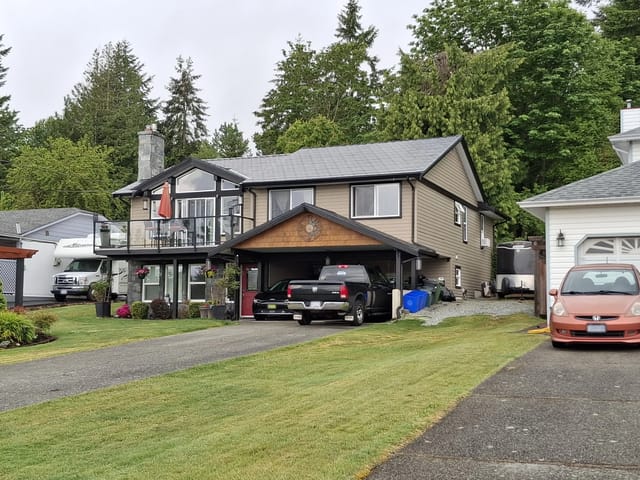 Black Interlock Slate aluminum roof on a brown two-storey home with dormers among tall trees, Chemainus, British Columbia