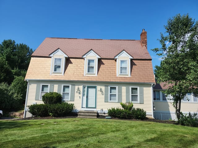 Aged Copper Interlock Shingle aluminum roof on a yellow two-storey Colonial home with dormers among tall, Wrentham, Massachusetts