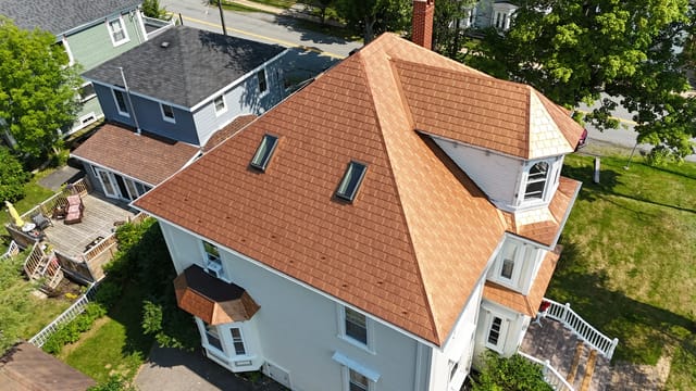 Aged Copper Interlock Slate aluminum roof on a white two-storey home with dormers among tall trees, Lunenburg, Nova Scotia