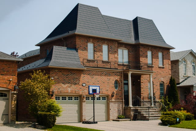 Two-storey brick Colonial home in Woodbridge ON with a complex multi-hip black Interlock aluminum slate metal roof and prominent Mansard-style lower sections.