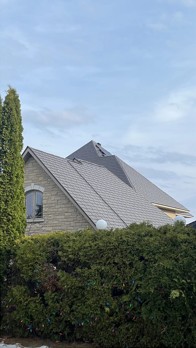 Tudor Brown Interlock Slate aluminum roof on a brown two-storey Tudor home with dormers among tall pines, Sudbury, Ontario