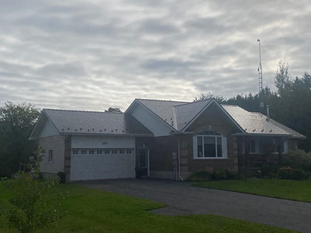 Ranch-style brick home in Winchester ON featuring Interlock Tudor Brown aluminum slate metal roofing with multi-gable complex roof profile under overcast skies.